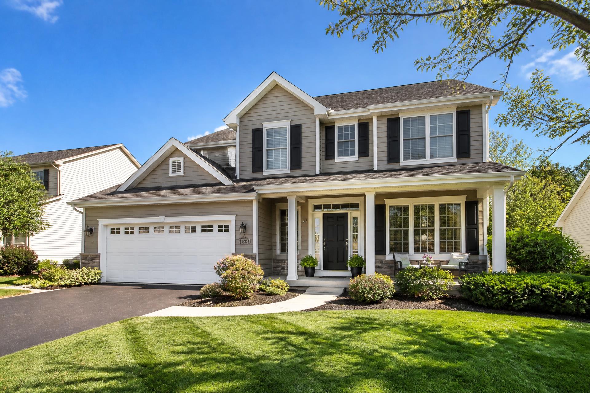 Beautiful modern suburban home with welcoming front porch and green lawn on a sunny day